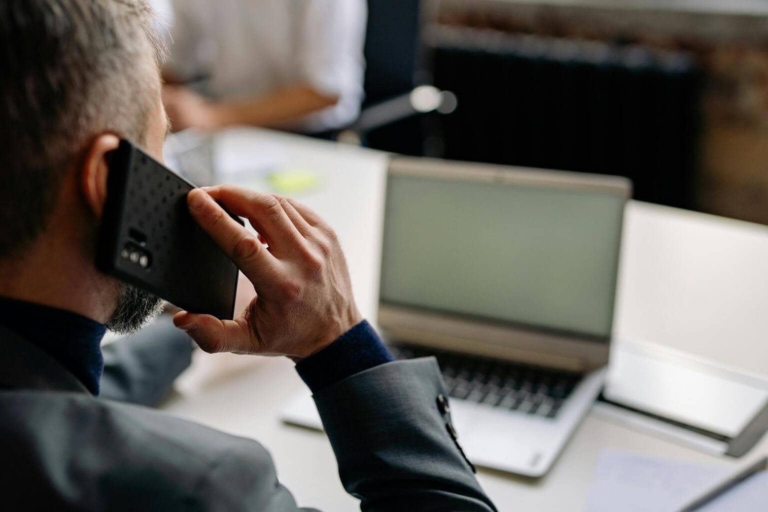 Muž v saku telefonuje u otevřeného notebooku